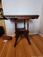 Front view of antique wooden parlour table showing carved details, turned legs, scalloped edges, and lower shelf.