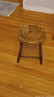 Full view of the antique wooden stool showing the seat and three legs on hardwood floor.