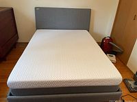 Full view of grey upholstered bed frame with foam mattress in bedroom setting