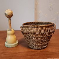 Wooden hat stand next to woven basket showing both items together on wooden table surface.