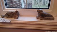 Two Inuit soapstone seal carvings placed side by side on a window ledge showing front and side angles
