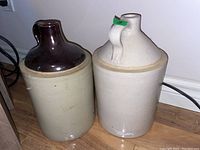 Photo showing two stoneware jugs side by side on the floor, one with dark brown glazed top and the other fully light beige.