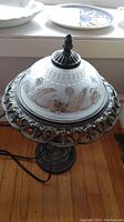 Front view of metal and glass table lamp showing floral etched glass shade and ornate metal base on hardwood floor
