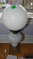 Full view of the milk glass oil lamp with round cracked milk glass shade, floral embossed milk glass body, and ornate metal base.
