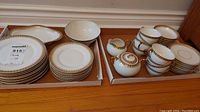 Full set of stacked Limoges china plates, cups, creamer, sugar bowl, all with gold trim on white porcelain.