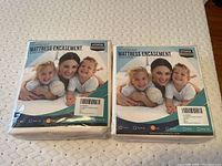 Photo of two new, full size waterproof mattress encasements in original packaging by Utopia Bedding on a mattress.