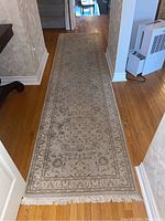 Full length view of hallway runner rug laid out on hardwood floor showing overall pattern and fringe at far end.