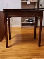 Front view of dark wood antique style card or game table showing drawer and table legs.