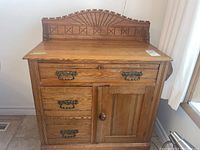 Front view showing three drawers with ornate metal handles and paneled door for storage.