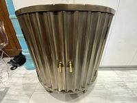 Front view of demilune cabinet showing corrugated metallic finish and double doors with gold-tone tassel handles.