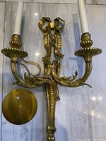 Overall front view of the gilt bronze Louis XV-style wall sconce with two candle-style lights and attached wiring, laid on marble surface.