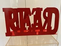 Front view of a large red metal book holder forming the word READ, showing thick metal letters and solid base.