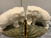 Pair of white elephant bookends on green and brown bases facing each other, showing the wear and split between the two halves.