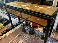 Overall view of the vintage Asian lacquer console table showing hand painted floral motifs on tabletop and drawer fronts, black lacquer frame, with some wear on paint edges.
