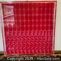 Front view of square acrylic pop art prototype B showing red and pink repeating oval and numeral pattern in clear acrylic frame