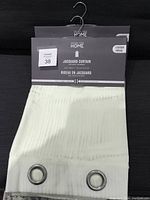 Two cream-coloured jacquard curtain panels with metal grommets, displayed with original packaging label Mathstays Home Jacquard Curtain.