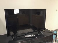 Photo of a 32-inch RCA flatscreen television placed on a black stand with an RCA remote control in front and a power cable coiled beside the remote.