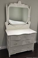Full view of antique white painted wooden dresser with three drawers and decorative carved mirror frame