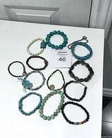 Photo displaying 13 assorted costume jewellery bracelets of various bead colors and styles arranged on a white surface in front of a door.