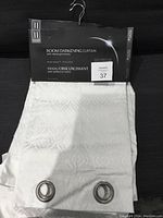 Photo of white curtain panel with attached label indicating room darkening curtain with metal grommets 38x84 inches