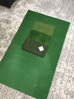 Two artificial turf golf mats laid on a carpeted floor. One large solid green mat, one smaller turf segment mat with three green turf variations.