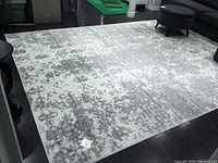 Photo of large rectangular grey and white area rug with an abstract mottled pattern placed on dark flooring in a living room setting.