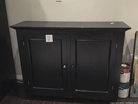 Front view of the black MDF cabinet with closed doors showing some paint wear.