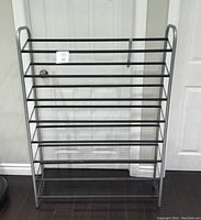 Front view of large metal shoe rack with 8 shelves against a white door showing overall design and size.