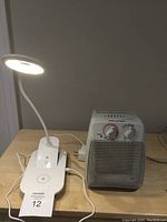 White LED ring light with flexible neck, wireless charging pad at base, next to a white ceramic heater with front grille and control knobs.