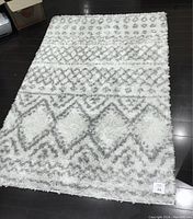 Photo of white and grey shag area rug laid flat on a dark floor showing geometric pattern and size