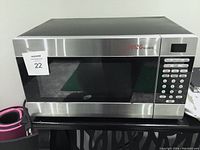 Front view of a stainless steel Living Basics microwave showing control panel and window.