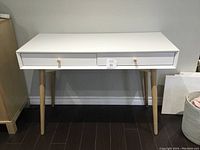 Front view of modern white desk with two drawers and natural wood tapered legs, showing overall condition and details.