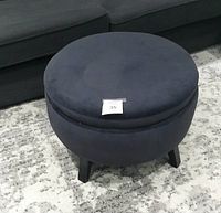 Front view of circular navy blue velvet ottoman showing cushioned top and black legs.