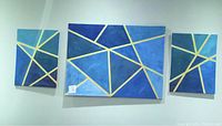 Three canvas paintings arranged on a white wall; one large rectangular canvas in the center with two smaller canvases on either side. All have blue backgrounds with gold geometric line designs.