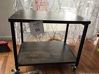 Full view of printer stand with wood-look laminate surfaces and black metal frame on wheels placed on hardwood floor.