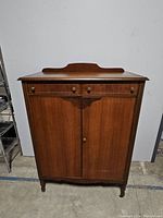 Closed view of antique wooden armoire showing three top drawers and two large doors below.