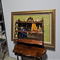Full front view of antique wooden shelf with mirrored back against a decorative framed background.