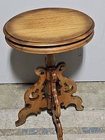 Full view of antique oval wooden table showing smooth two-tone top and ornate carved pedestal base.