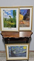 Photo showing three framed art prints on and above a wooden table: Claude Monet style landscape, Van Gogh The Cafe Terrace at Night, and Starry Night.