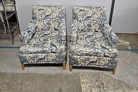 Pair of patterned upholstered armchairs with wooden legs shown front view on concrete floor.