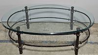 Oval coffee table with clear glass top and iron metal base, viewed from the side.