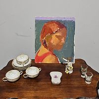 All items displayed on wooden surface including painted portrait, porcelain cups stacked, figurine, small dish, and glass cups.