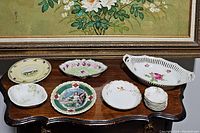 Photo of all decorative plates and bowls arranged on a wooden table under a painting.