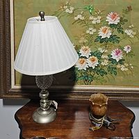Full view of white shade lamp with metal and glass base on wooden table