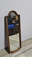 Front view of the full-length arched mirror leaning against a white wall, showing wood frame and scratches on glass.