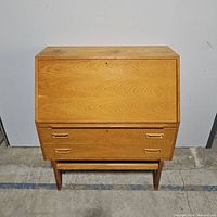Front view of wooden secretary desk showing drop-front closed and two bottom drawers