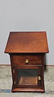 Front view of wooden side table showing drawer and closed glass door cabinet below.