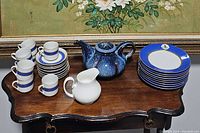 Full view of tea set items arranged on dark wooden table showing cups, saucers, plates, teapot, and creamer pitcher