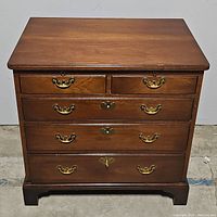 Front view of the vintage wooden chest showing five drawers with brass handles and keyholes.