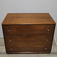 Front view of the wooden chest showing three closed drawers and metal knobs.